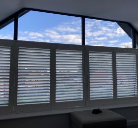 Uk manufactured faux wood shutters in silk white, 64mm Louvre and clear view tilt installed to this gable window.: Click Here To View Larger Image